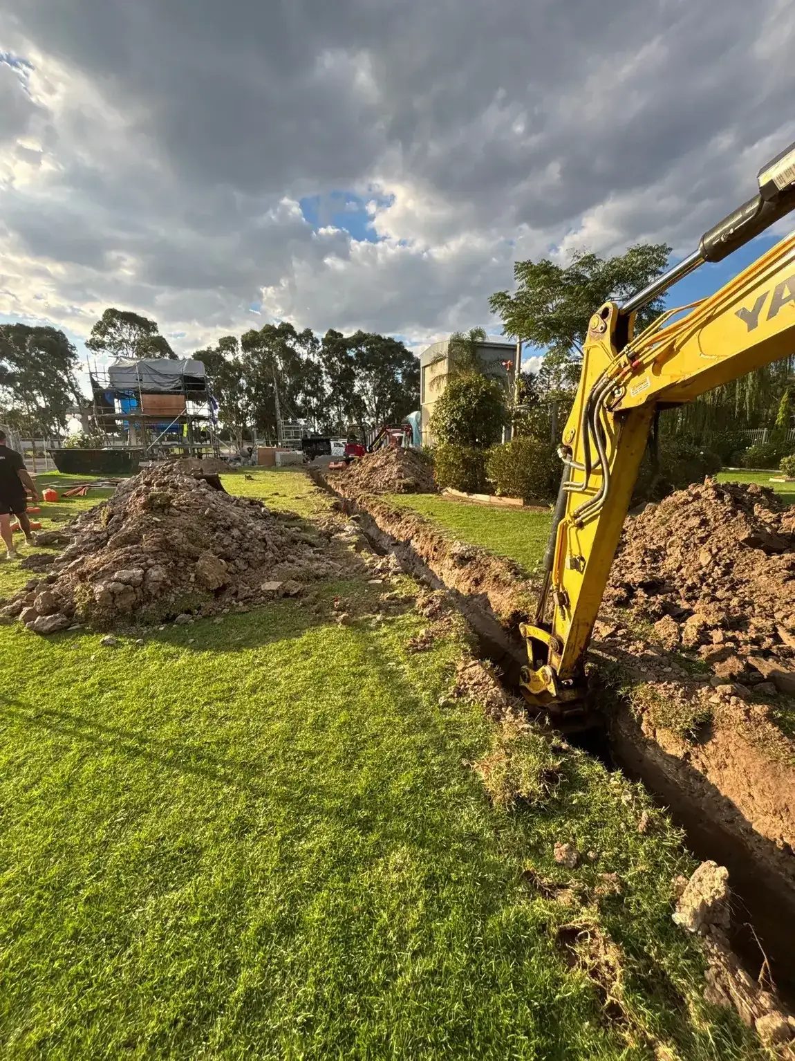Excavator cutting a drainage trench across a commercial site