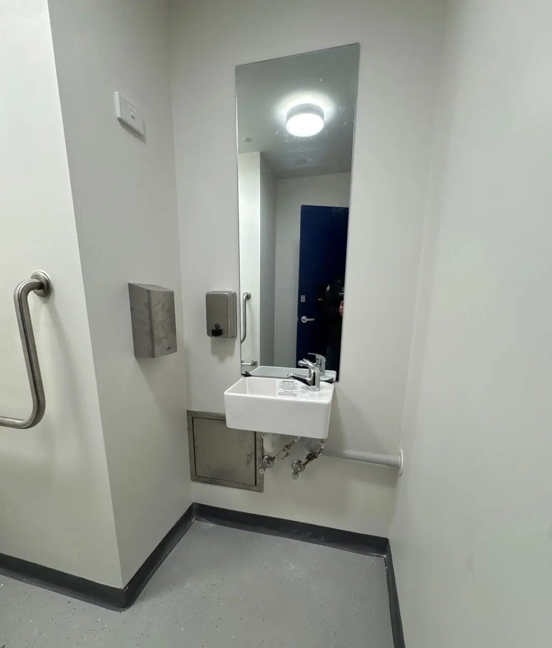 Wall-hung basin, tapware and service access panel in a completed public amenity