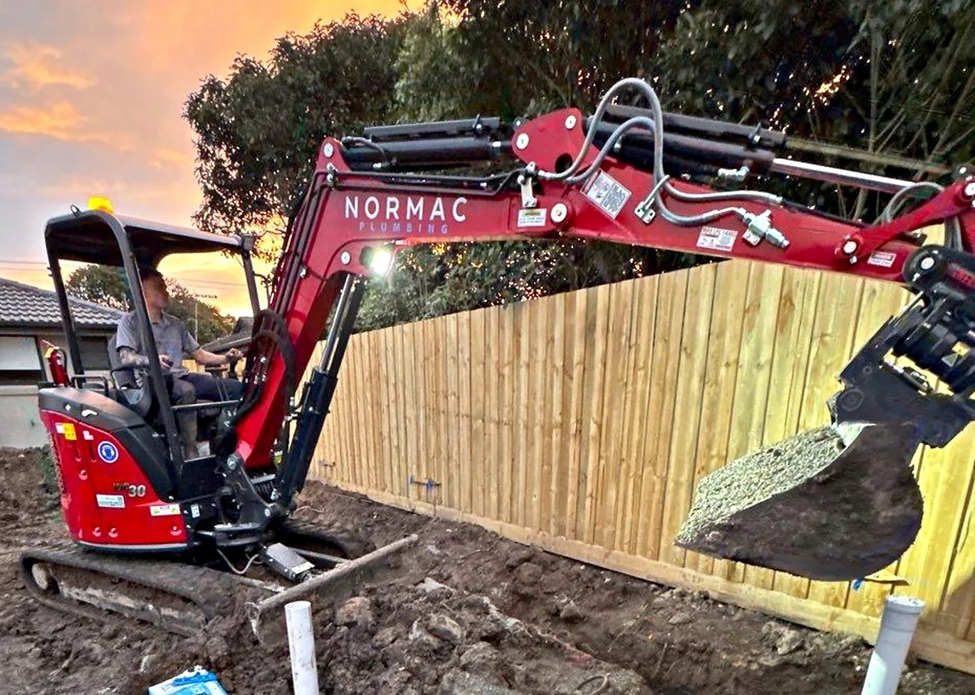 Normac Plumbing excavator over a new sewer and stormwater rough-in at dusk