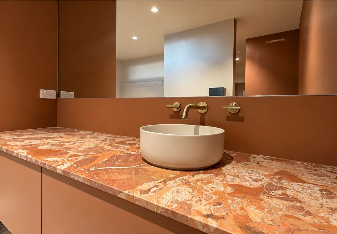 Above-counter basin with wall-mounted brass tapware on a stone benchtop