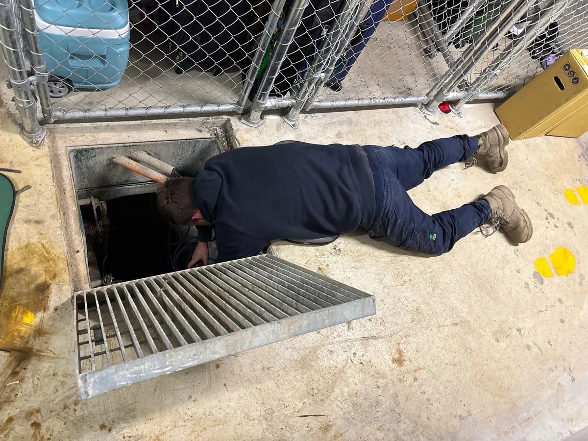 Plumber accessing an in-ground pit beneath a removed grate on a commercial site